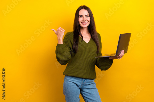 Photo of pretty shiny woman dressed khaki sweater working modern device pointing thumb empty space isolated yellow color background