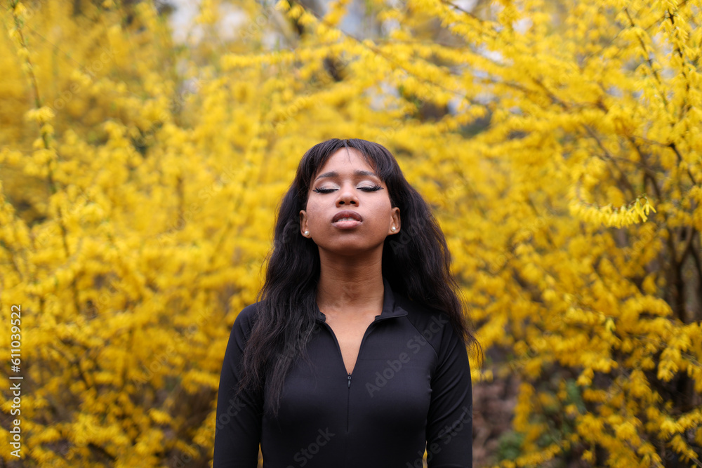 Beautiful long haired african american girl with closed eyes enjoys the smell of blooming yellow forsythia bushes in the city park. Beautiful long haired african american girl with closed eyes enjoys the smell of blooming yellow forsythia bushes in the city park.