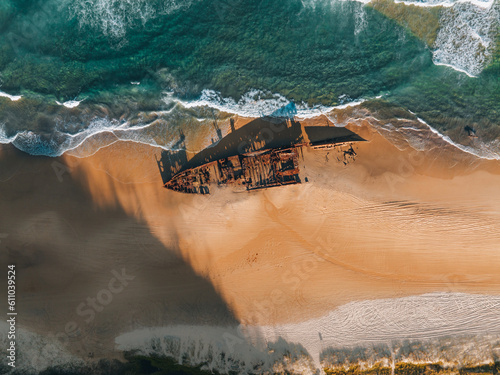 K'gari High angle aerial bird's eye drone view of the Maheno shipwreck on Seventy-Five Mile Beach on Fraser Island, Queensland, Australia. Beautiful sunset light with waves.