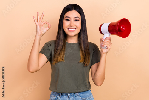 Portrait of charming positive girl beaming smile hold loudspeaker demonstrate okey symbol isolated on beige color background