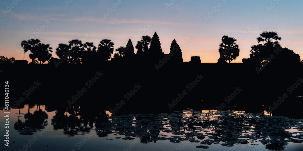 Fototapeta premium Experience the ethereal charm of Angkor Wat at dawn, where the dark sky and tree silhouettes add a touch of mystique to the Cambodian landscape.