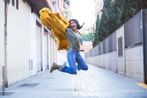 Adult woman in a yellow coat jumps on an urban street © EvaHM