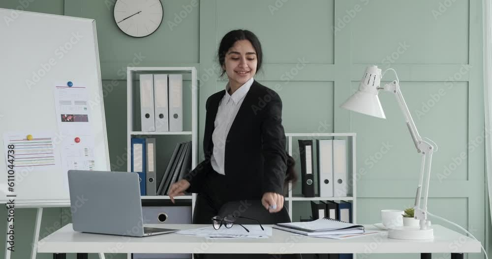 Indian woman exuding positive energy as she dances with enthusiasm near her office desk. In a vibrant and upbeat atmosphere, she moves gracefully, radiating joy and happiness.