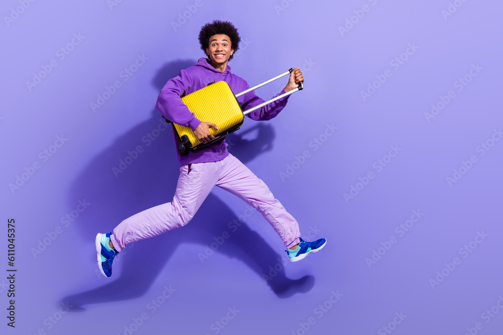 Full size photo of funny funky handsome person dressed violet hoodie pants hold valise run to airport isolated on purple color background