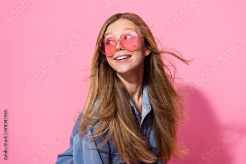 Photo portrait of pretty young teen girl fluttering hair look empty space dressed stylish denim outfit isolated on pink color background