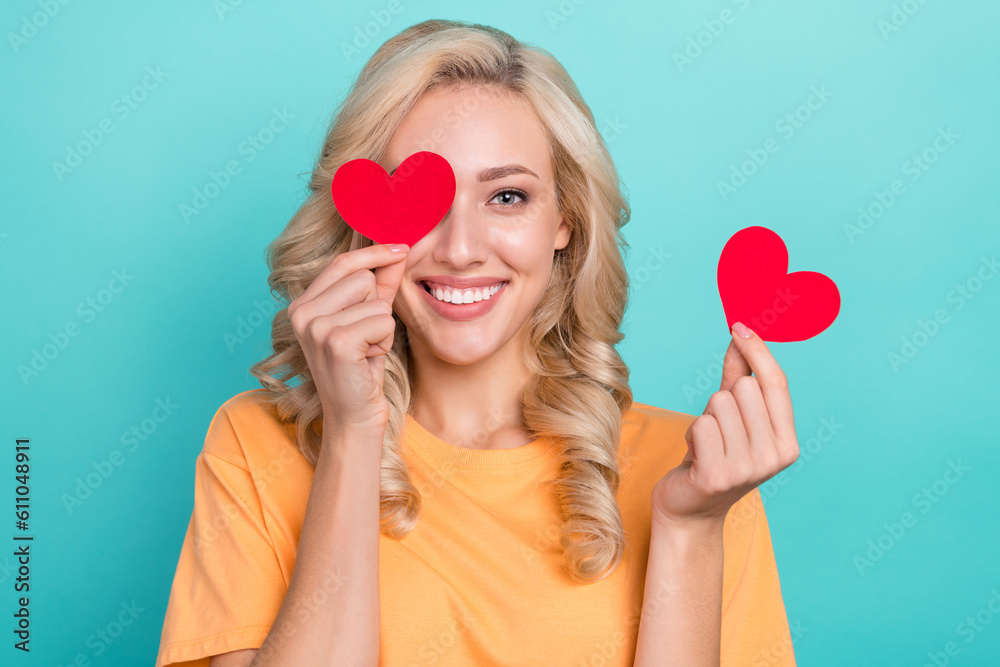 Portrait of good mood person wear stylish t-shirt fingers hold red paper hearts postcards cover eye isolated on turquoise color background Portrait of good mood person wear stylish t-shirt fingers hold red paper hearts postcards cover eye isolated on turquoise color background