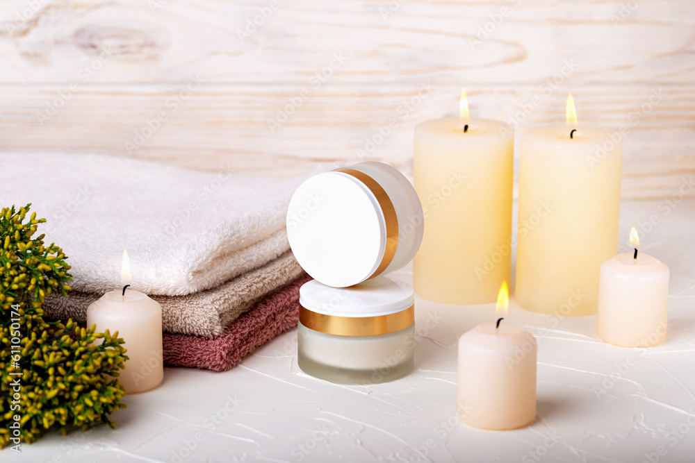 Jars with day and night face cream, burning candles, towels and juniper branch on light background. Cosmetic skin care, spa procedures. Concept of calmness, comfort. Selective focus Jars with day and night face cream, burning candles, towels and juniper branch on light background. Cosmetic skin care, spa procedures. Concept of calmness, comfort. Selective focus