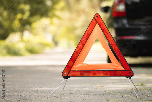 Red triangle, red emergency stop sign and black car with technical problems in the blurred background. Emergency stop of the car on the road. Safety procedure while having a vehicle broken down