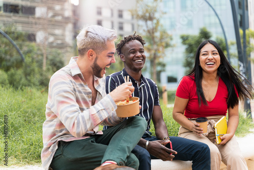Fotografie Young multiracial friends eating take-out street food in the city park during jo