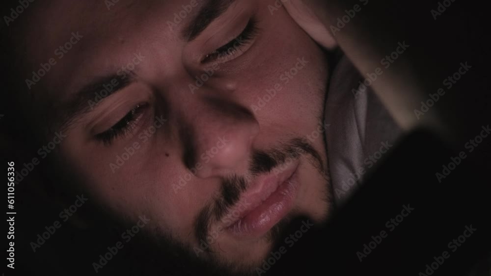 Night movie. Gadget insomnia. Tired restless bored man watching video show online on mobile phone lying in bed in dark with blue flicker light.