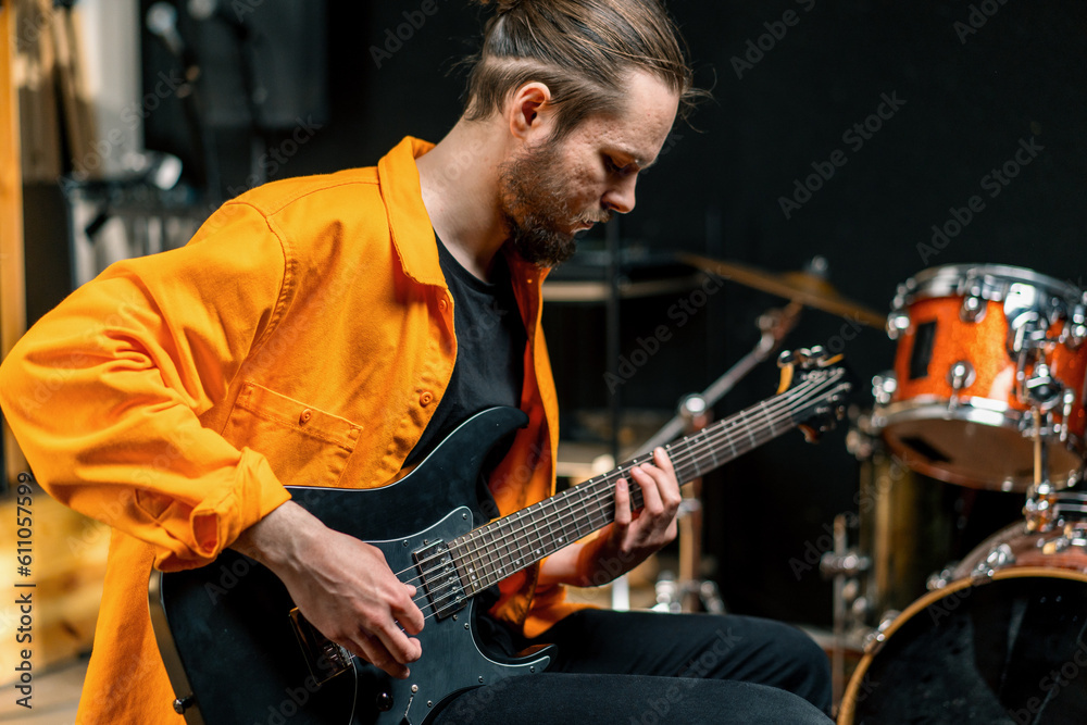 Obraz premium portrait of young rock artist with electric guitar in recording studio playing own track musical instrument drums on background