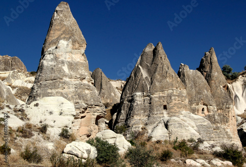 Landscape with mushroom-shaped mountains (also called Fairy Chimneys) with caves inside against a bright blue clear sky in the Zemi Valley near the town of Goreme in Cappadocia, Turkey