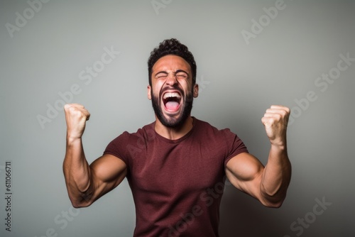 Medium shot portrait photography of a happy boy in his 30s celebrating with his fists against a minimalist or empty room background. With generative AI technology