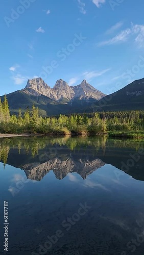 Mountain peaks reflecting in the calm water below at Three Sisters in Canmore, near Banff National Park, Canada in summer time with wilderness, wild, tourist, tourism area.