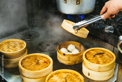 A pair of tongs holds open a Chinese steamer containing bao dumplings on a stovetop