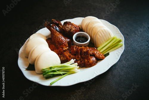 Peking duck with chinese pancakes, scallions and a dipping sauce on a white platter against a black background photo
