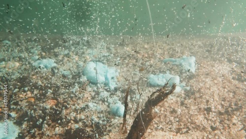 Paper scraps fall down and not melting in lake water with pebbled bottom polluting pond. Chemical pollution on lake biome. Environment care concept photo