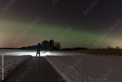 Frozen winter lake with sled track and figure with headlamp under night sky with aurora activity