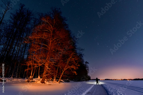 Frozen winter lake with sled track and figure with headlamp under night sky