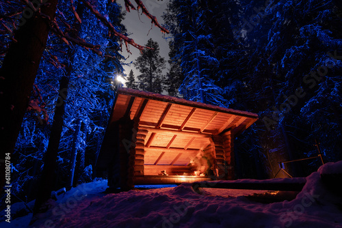 Shelter in firelight in winter forest with blue light in background under full moon