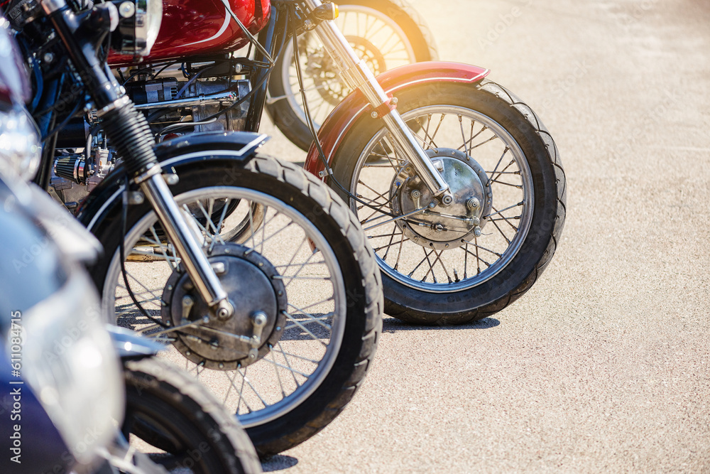 Obraz premium Motorcycle front wheels close-up. Motorcycles stand in a row on the sidewalk, side view. Motorcycles are parked in the motorcycle parking area.