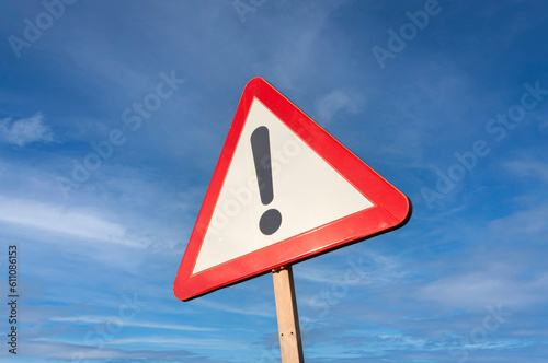 Warning road sign with exclamation mark, against a blue sky background.