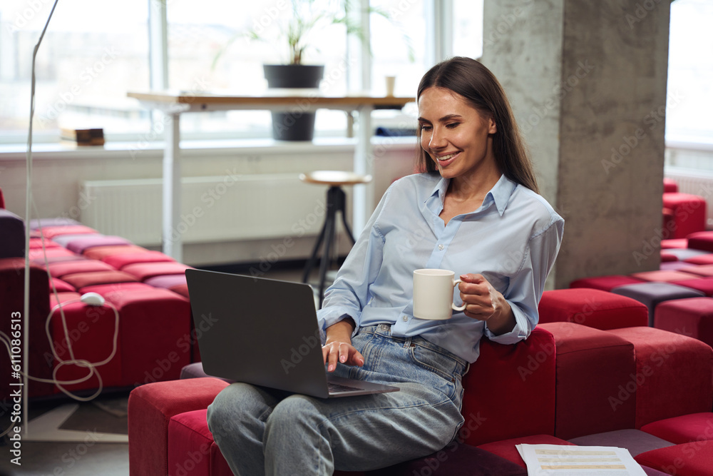 Joyful female freelancer using her laptop during tea break indoors