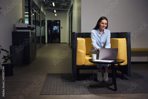 Joyous female office employee working on computer during coffee break
