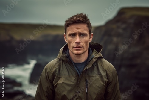 Headshot portrait photography of a glad boy in his 30s wearing a lightweight windbreaker against a dramatic coastal cliff background. With generative AI technology