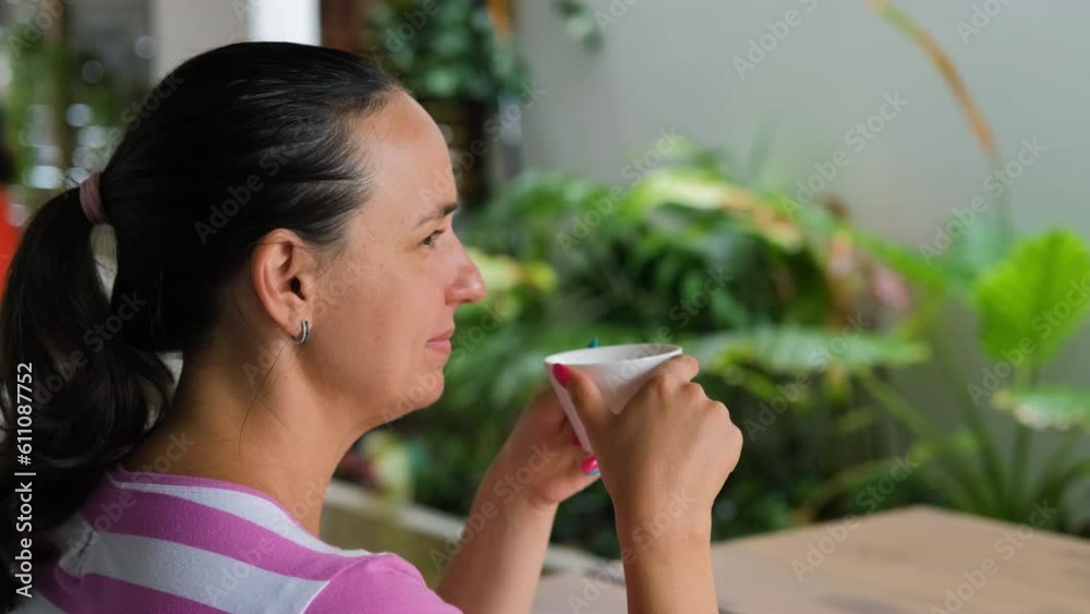Cheerful young woman drinking fresh coffee while sitting at table on green tropical terrace of hotel or cafe Cheerful young woman drinking fresh coffee while sitting at table on green tropical terrace of hotel or cafe