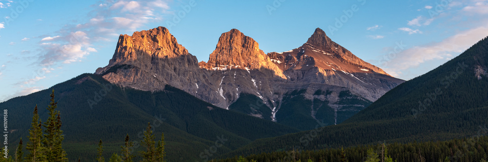 Golden sunset peaks near Banff National Park with Three Sisters at Canmore in view. Sun shining bright on the stunning panoramic view of wilderness, nature scenery in Canada.