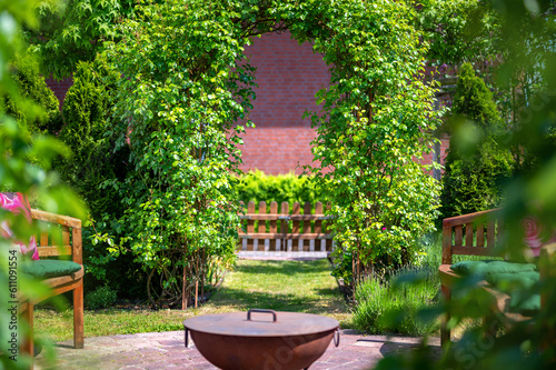 Traumhaft schön angelegter Garten mit einem Rosenbogen und einer Sitzgruppe mit Feuerschale