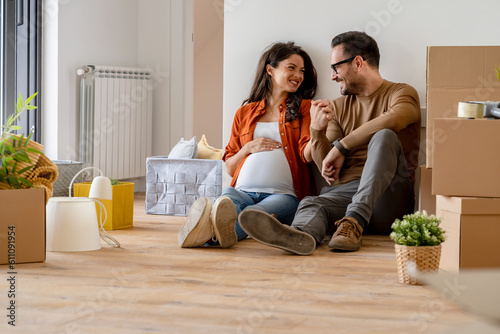Photos A young happy married couple expecting a baby sitting on the floor of their new home after moving in