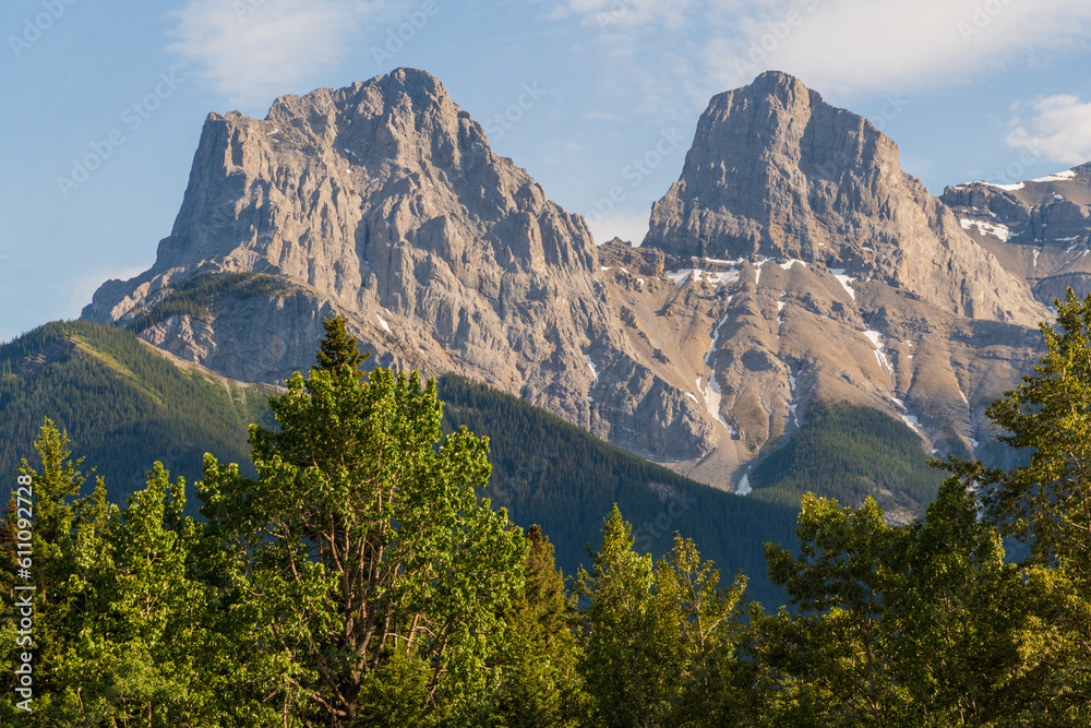 Three Sisters in Canmore seen at golden hour, sunset with mountain peaks shining bright with sunshine. Beautiful, pristine, famous, tourist area, Banff National Park. 