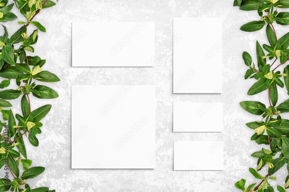 Naklejka premium Composition of leaves and white watercolor sheets of paper on gray concrete background. Tree branches with leaves, blank cards. Nature mockup, ecology poster. Top view, flat lay, close up, copy space