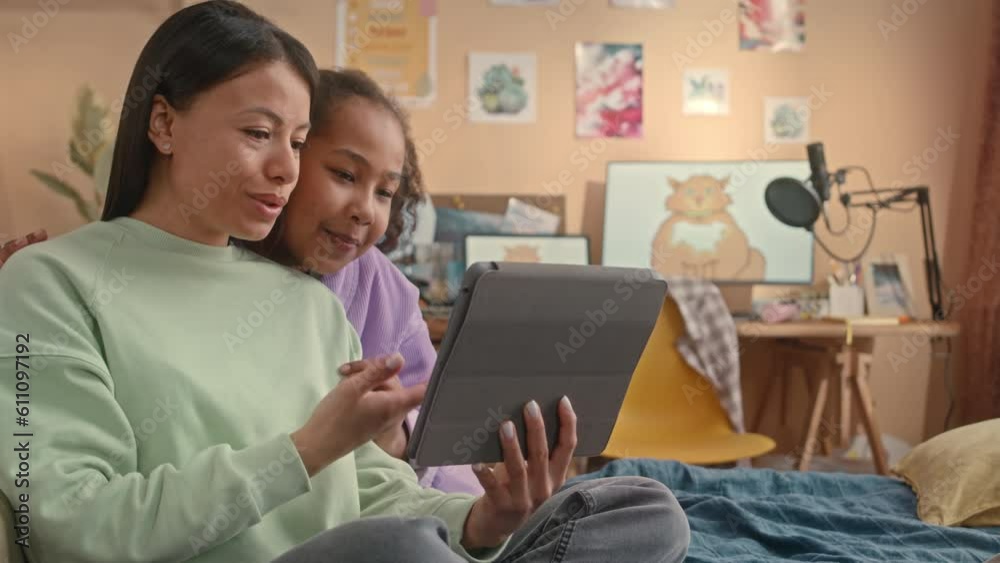 Waist up of African American young mother and preteen daughter waving and smiling at digital tablet screen while having video chat from home Waist up of African American young mother and preteen daughter waving and smiling at digital tablet screen while having video chat from home