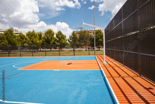 Empty outdoor basketball court in the garden and blue sky. Blue red basketball court for soccer, outside in sunny summer day. A modern playground for sports without people. Playground flooring. © vita