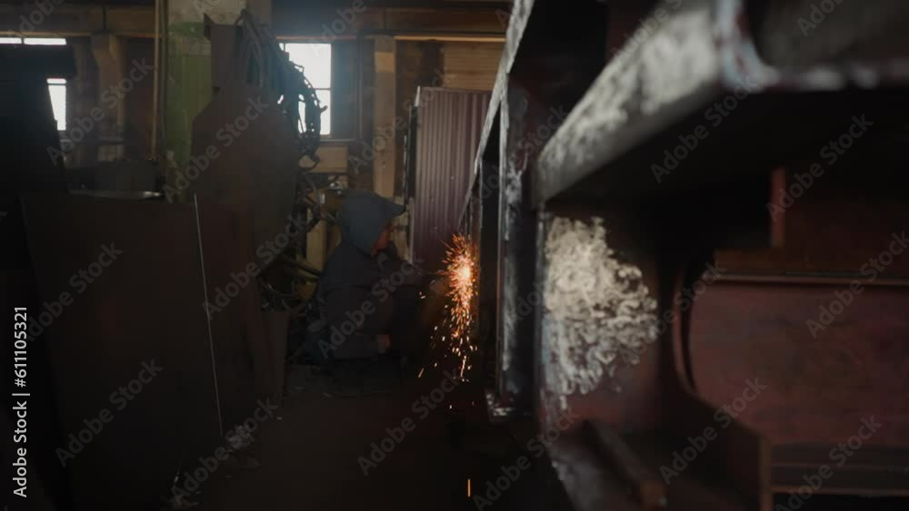 Fire sparks fly during welding of large metal construction in plant workshop closeup. Flashing flame by attached steel beams at metalworking factory Fire sparks fly during welding of large metal construction in plant workshop closeup. Flashing flame by attached steel beams at metalworking factory