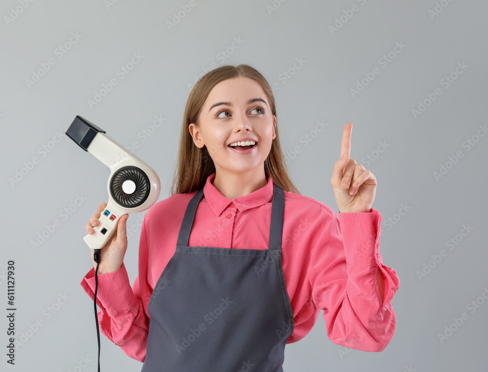 Female hairdresser with dryer pointing at something on grey background Female hairdresser with dryer pointing at something on grey background