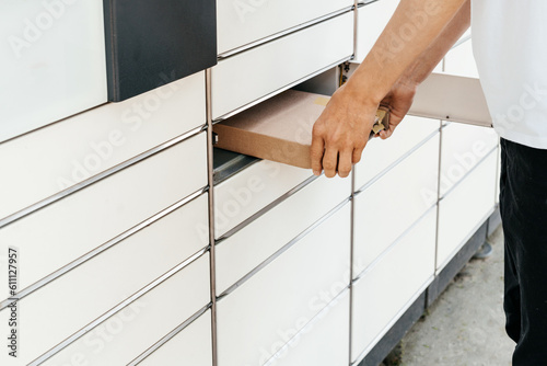 A man with a box in his hands near the self-service mail terminal. Parcel delivery machine. Person holding a cardboard box. Mail delivery and post service, online shopping, e commerce concept 