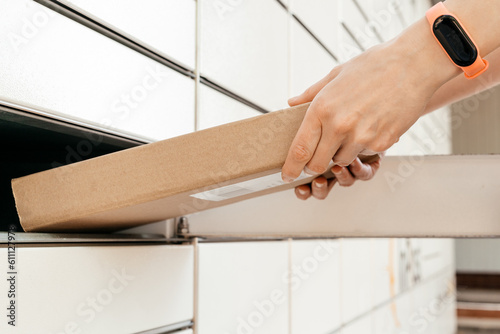 A woman with a box in his hands near the self-service mail terminal. Parcel delivery machine. Person holding a cardboard box. Mail delivery and post service, online shopping, e commerce concept