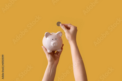 Картината върху платно Woman with coin and piggy bank on yellow background