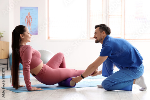 Young woman training with foam roller and physiotherapist in rehabilitation center
