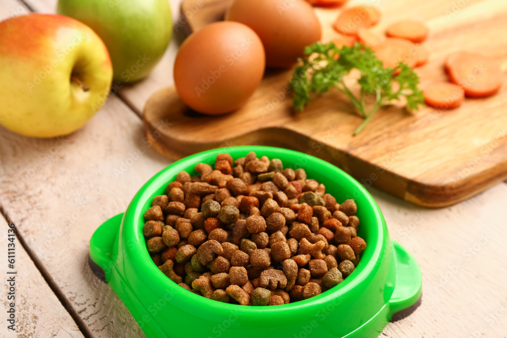 Bowl with dry pet food and natural products on light wooden background, closeup Bowl with dry pet food and natural products on light wooden background, closeup