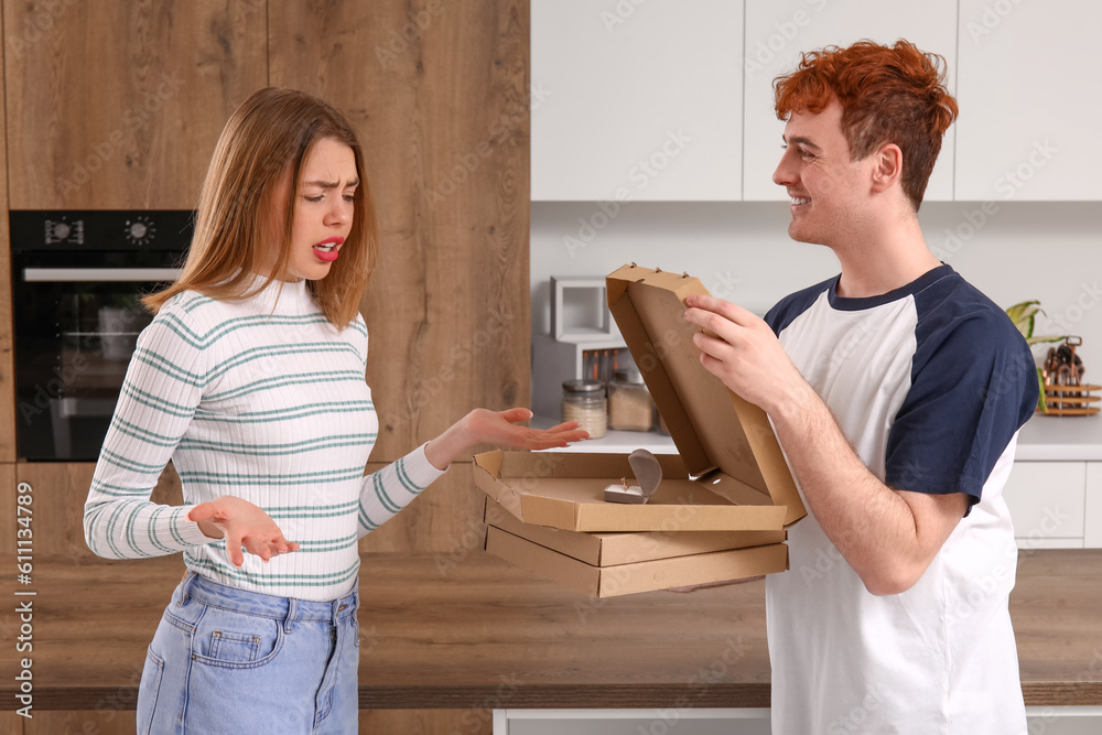 Young man with pizza proposing to his confused girlfriend in kitchen Young man with pizza proposing to his confused girlfriend in kitchen