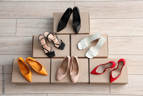 Cardboard boxes with different colorful high-heeled shoes on light wooden background