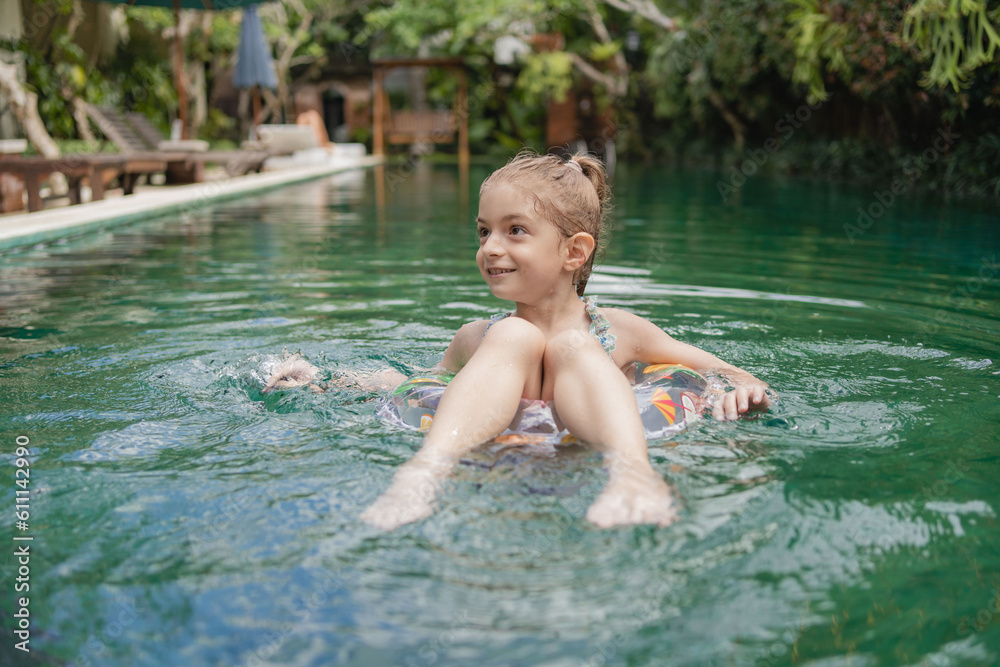 Cute little girl with inflatable ring in tropical pool resort