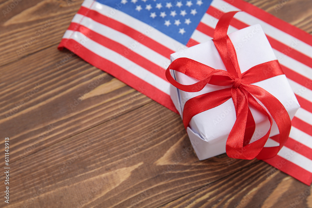 Fototapeta premium Gift box with USA flag on brown wooden background. American Independence Day