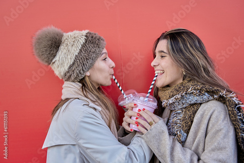 two friends drinking a smoothie or strawberry milkshake on a red background