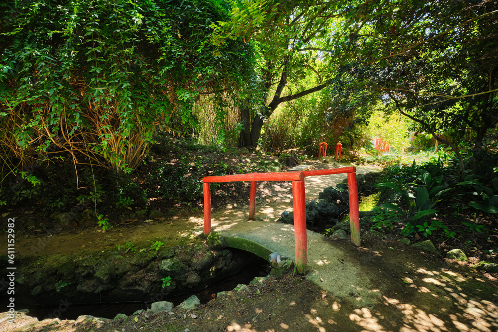 Red Chinese style bridge with wooden railings in lush greenery of asian part of tropical botanical garden in Lisbon, Portugal Red Chinese style bridge with wooden railings in lush greenery of asian part of tropical botanical garden in Lisbon, Portugal
